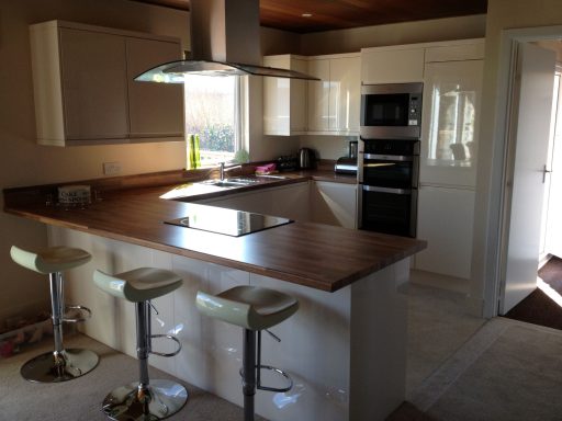 Modern kitchen with a wooden island, bar stools, and appliances in neutral tones.