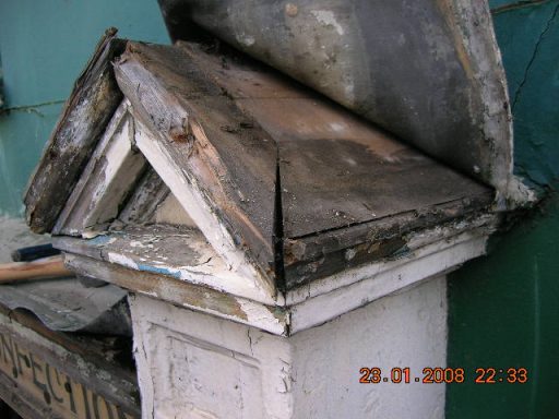 Damaged wooden structure with a slanted roof, showing decay and wear.