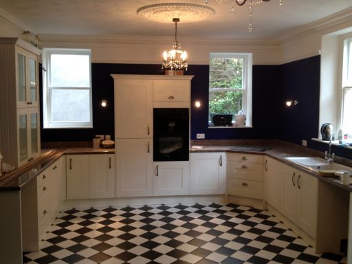 Modern kitchen with white cabinetry, black-and-white checkerboard floor, and natural light.