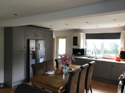 Modern kitchen with grey cabinets, wooden dining table, and large window.